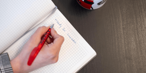 Hand holding pen and making a note in a notebook about innovation.