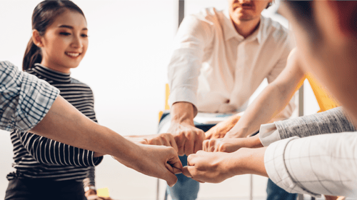 People standing in a circle putting their fists together. Blogpost about encouraging innovation in the workplace.