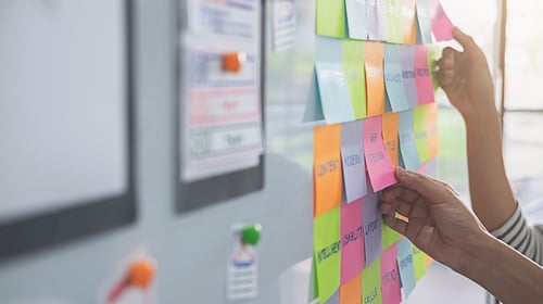 People brainstorming for a strategy plan. Colorful sticky notes with things to do on office board. 
