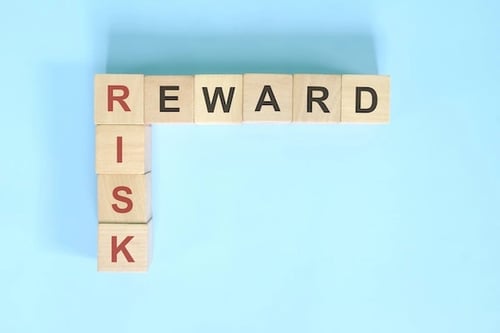 Photo of wooden blocks on flatlay blue background. Words 'Risk' and 'Reward' written on the blocks.