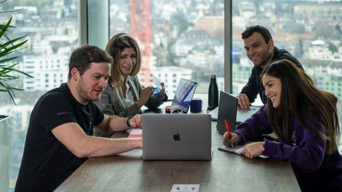 People sitting around a table looking at a laptop. Blogpost about corporate entrepreneurship types.