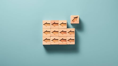 Arrows carved on wooden blocks facing in one direction with one arrow pointing into another direction talking about disruptive innovation