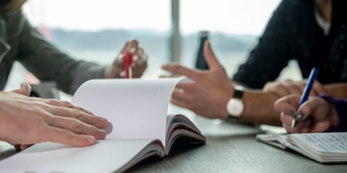 People sitting around a table working together close-up of hands and books.