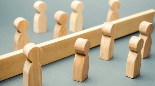 Wooden figures of people are separated by a barrier for a blogpost talking about the barriers of intrapreneurship. 