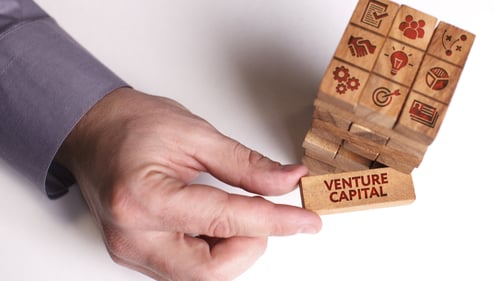 Man pulls venture capital block from a stack of blocks. Blogpost about Corporate Venture Capital Advantages and Disadvantages.